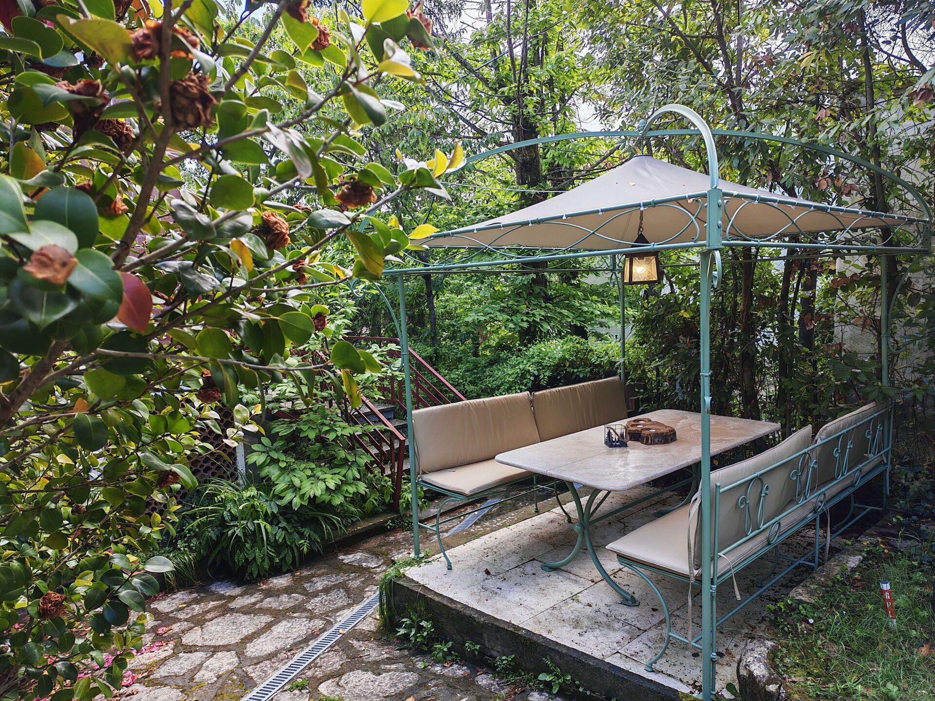 Un espace extérieur abrité, aménagé avec une table et des bancs, et entouré d’une végétation luxuriante.