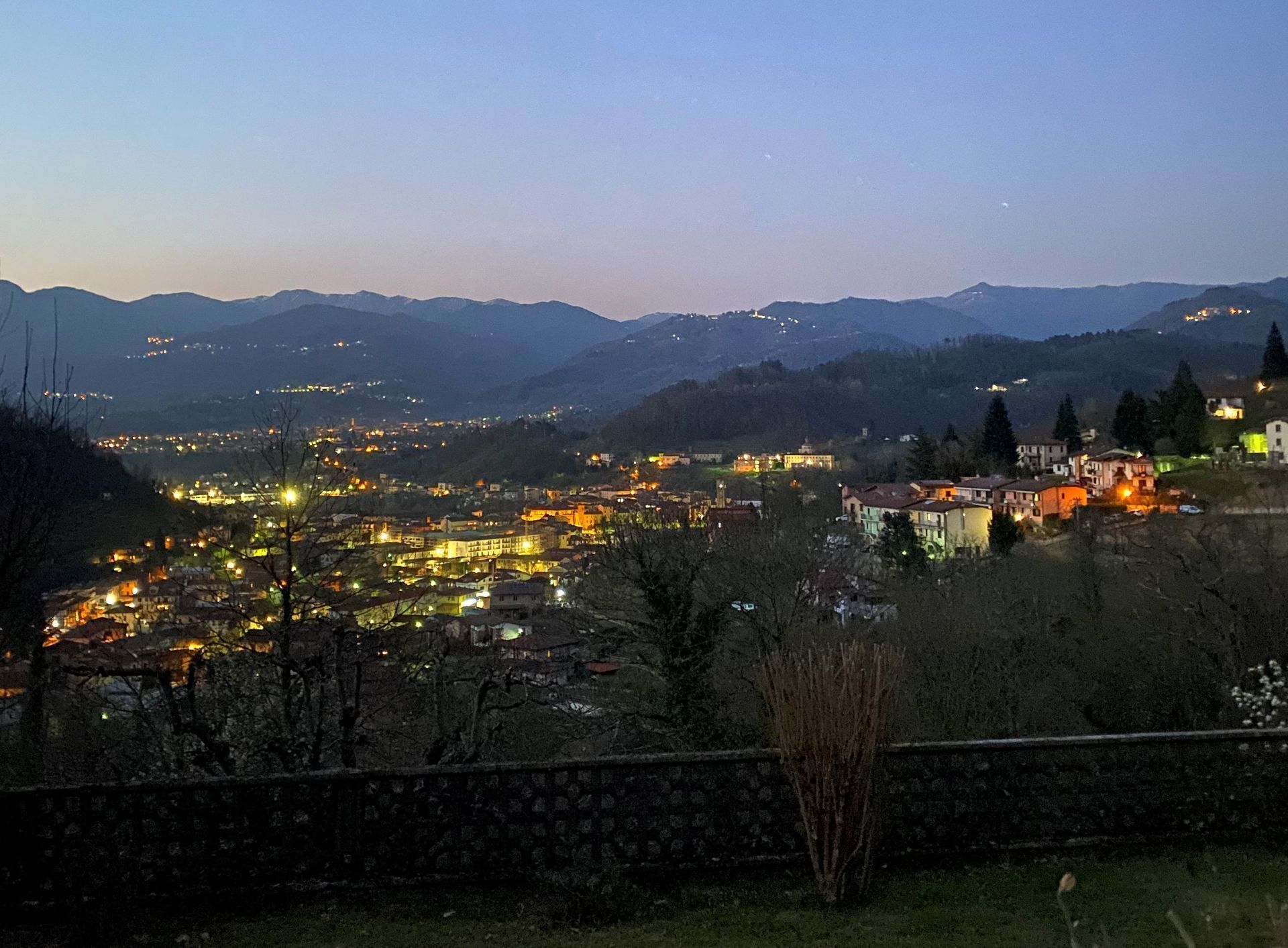 Une ville au crépuscule, avec des bâtiments illuminés et des montagnes en arrière-plan.