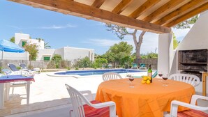 Un patio exterior con piscina, sillas blancas y una mesa con mantel naranja.