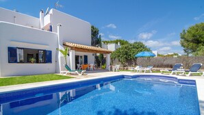 Un área de piscina moderna con una piscina azul cristalina, sillas de descanso y un patio con mesa y sillas.