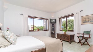 Un dormitorio con cama, cómoda, televisor y ventana con cortinas.