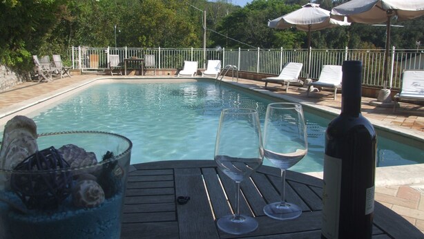 Area piscina con lettini, un tavolo con bicchieri da vino e una bottiglia, e ombrelloni.