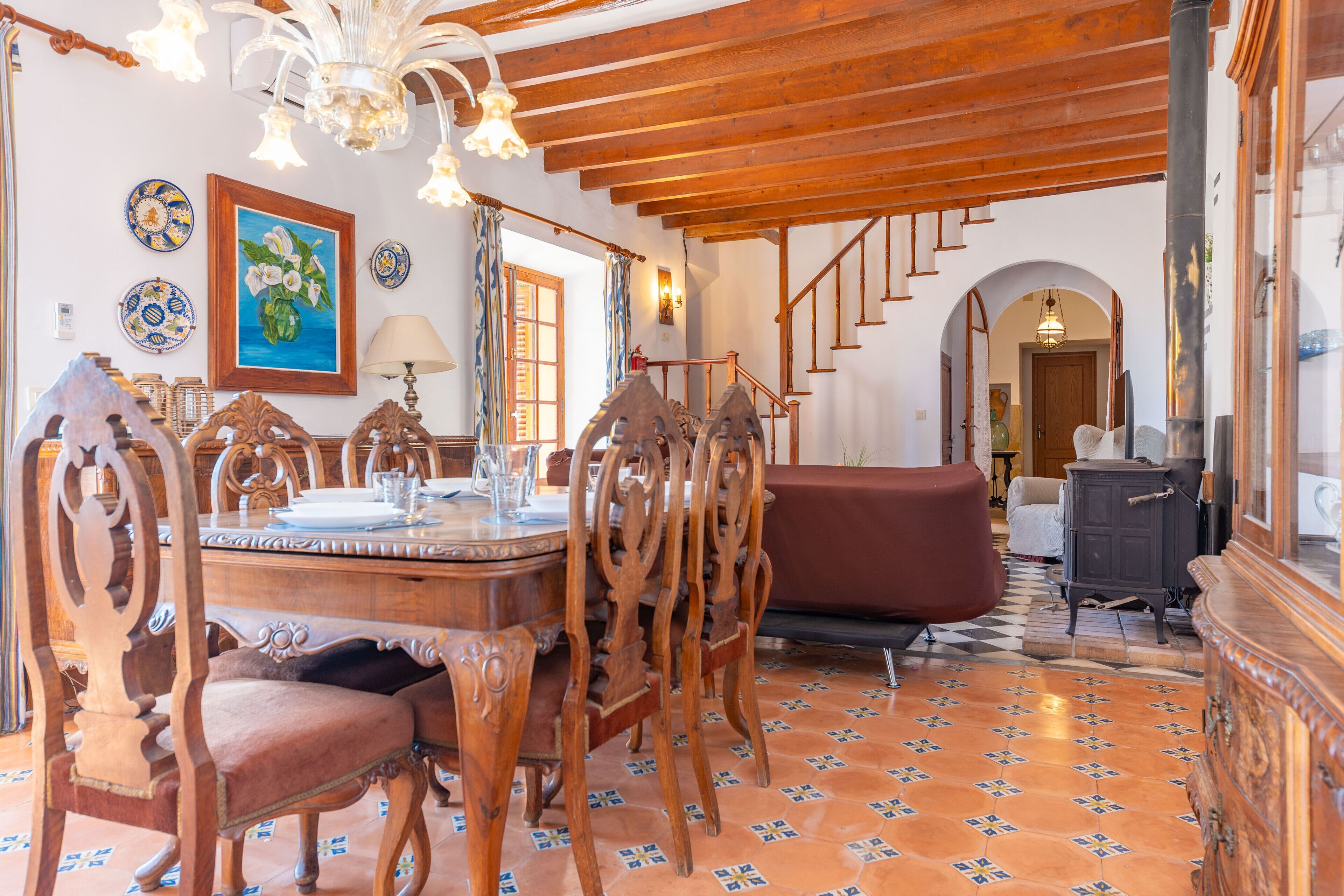 A dining area with a wooden table and chairs, a painting on the wall, and a staircase leading to another room.