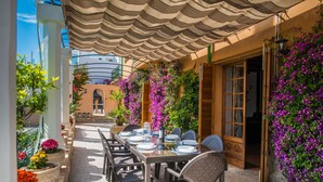 An outdoor dining area with a covered table and chairs, surrounded by potted plants and flowers.