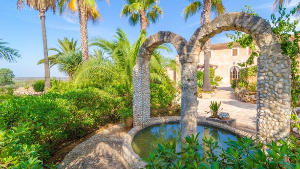 A garden with a stone archway, palm trees, and a small pond. - CAN PUÇA - Villa with private pool in Santanyí. Free WiFi (Santanyí)