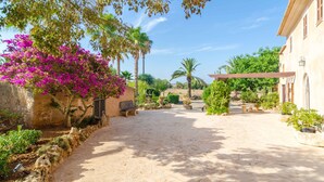 A courtyard with a stone pathway, a building with a balcony, and various plants including bougainvillea. - CAN PUÇA - Villa with private pool in Santanyí. Free WiFi (Santanyí)