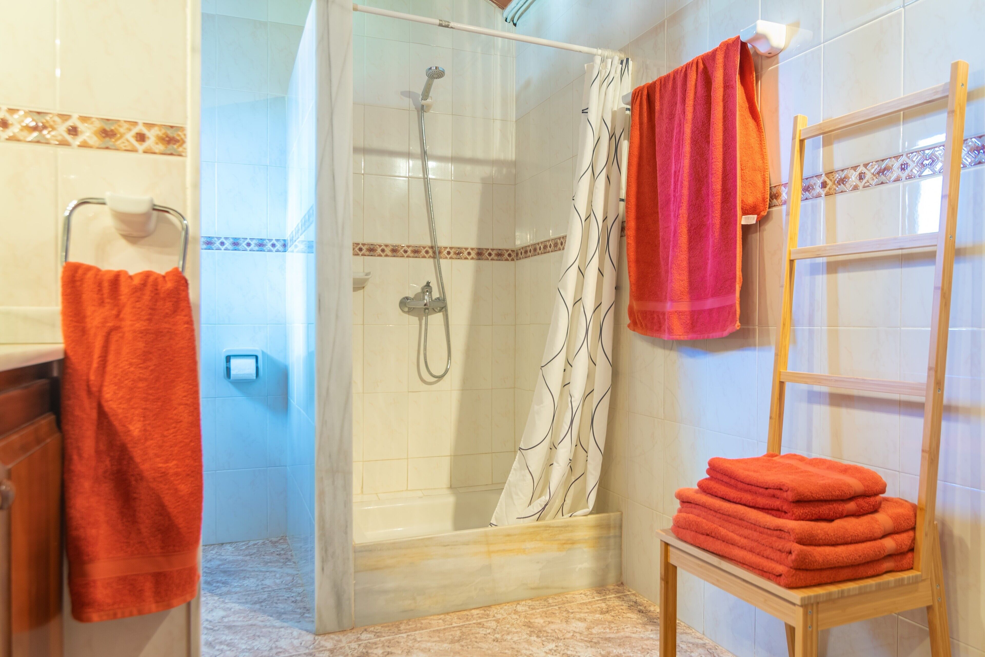 A bathroom with a shower, a towel rack, and a stack of towels on a wooden shelf.
