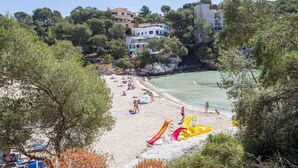 A beach with people sunbathing and playing, a yellow slide, and buildings in the background. - CAN PUÇA - Villa with private pool in Santanyí. Free WiFi (Santanyí)