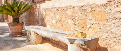 A rustic wooden bench with a chessboard attached, positioned against a textured stone wall.