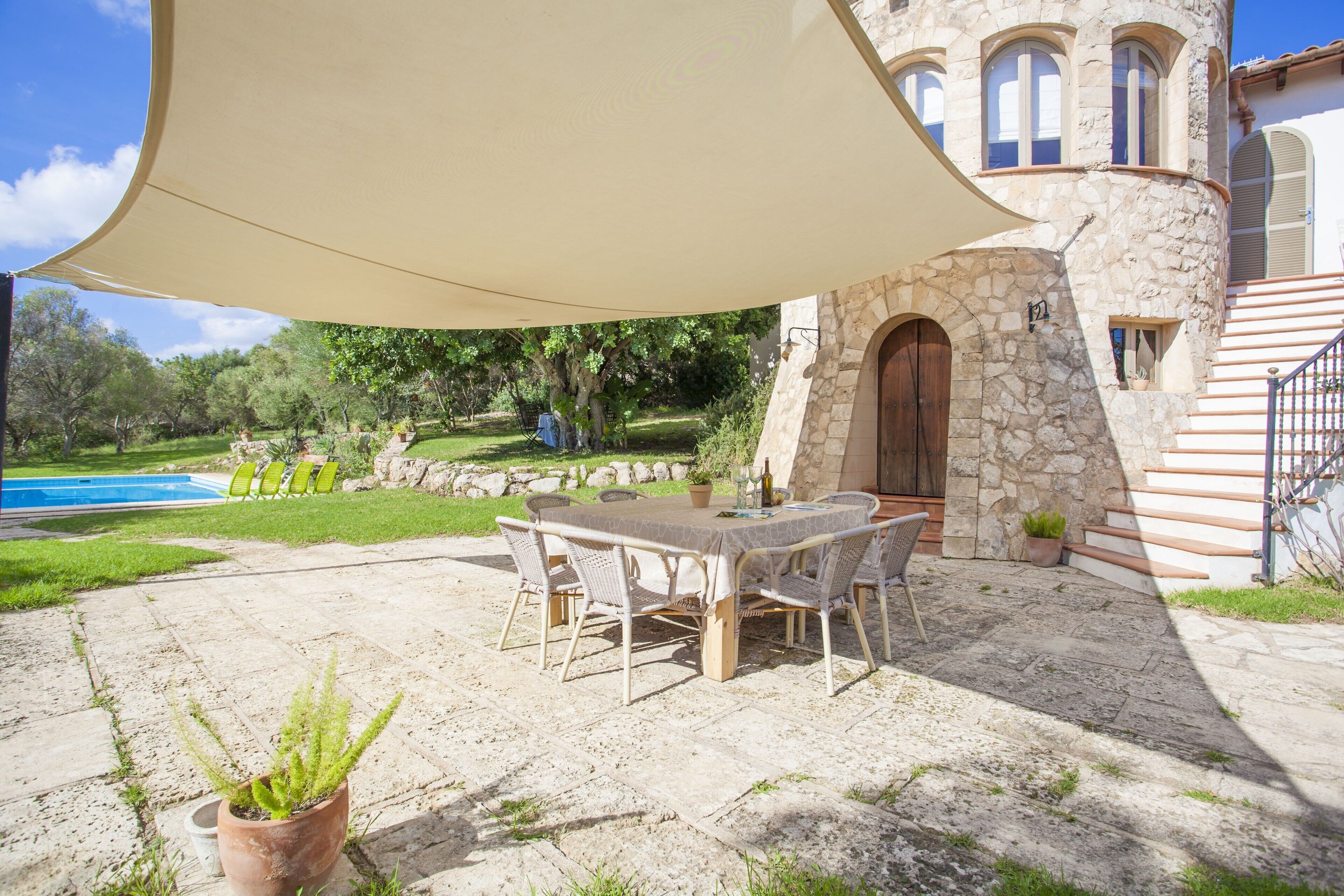 An outdoor patio with a table and chairs, a stone building, a pool, and greenery.