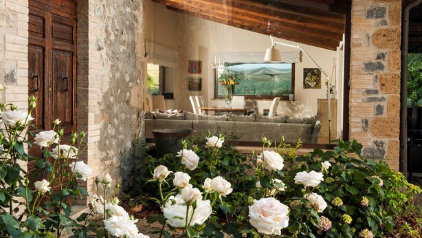 Un salon rustique avec un mur en pierre, une porte en bois et un canapé placé face à une grande fenêtre.