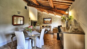 Un coin repas agrémenté d’un mur en pierre, de poutres en bois, d’un tableau et d’une table mise pour deux personnes.