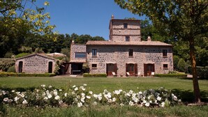 Un bâtiment en pierre doté d’une tour centrale, de nombreuses fenêtres et d’un jardin bien entretenu agrémenté de fleurs blanches.
