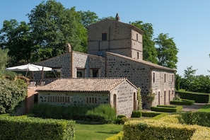 A stone building with a tower, surrounded by well-maintained hedges and trees.