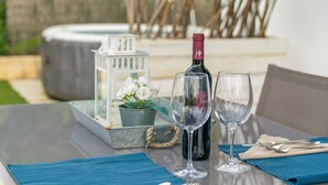 Una mesa dispuesta con una botella de vino, dos copas de vino, una casa decorativa blanca y una planta en maceta.
