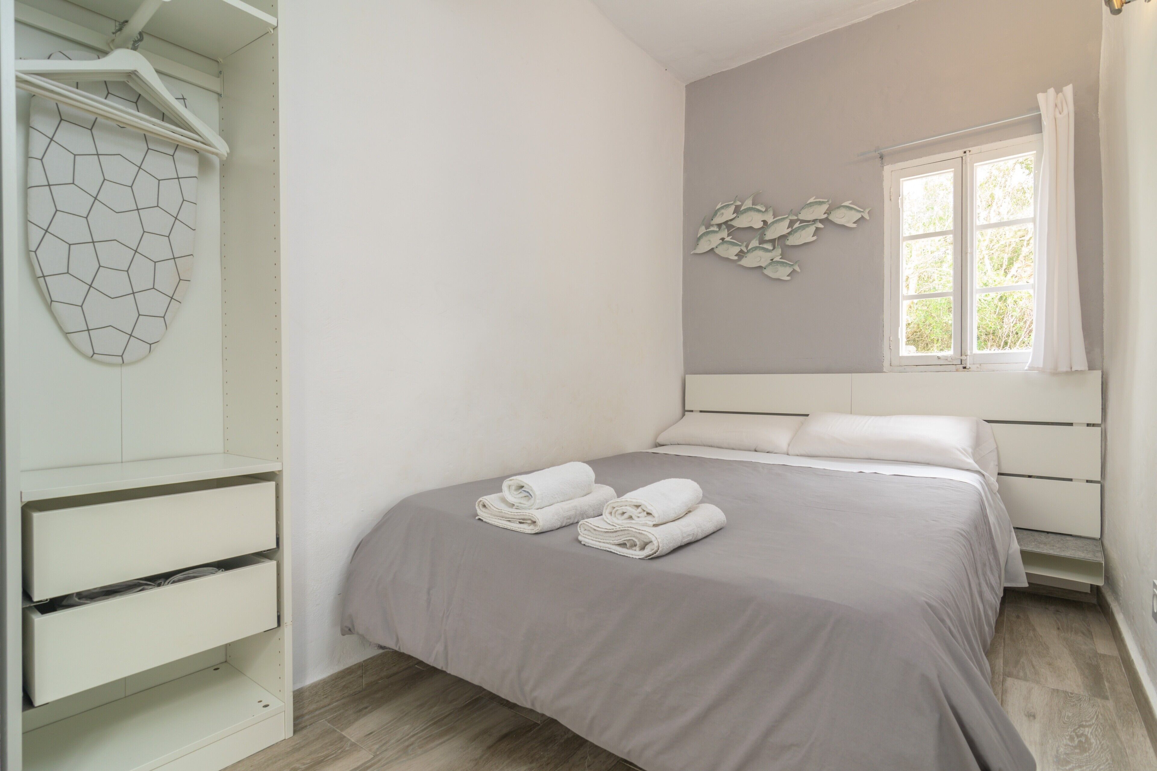 Quarto com cama, guarda-roupa, janela e um objeto decorativo na parede.