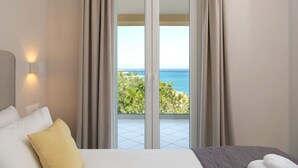 Une chambre d’hôtel avec un lit, une table de chevet, une lampe et une vue sur la mer, visible à travers une porte-fenêtre coulissante.