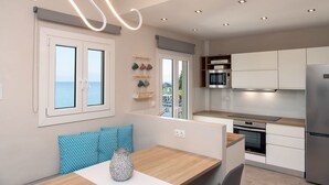 Une cuisine moderne avec des meubles blancs, des appareils en acier inoxydable et une vue sur la mer par une fenêtre.