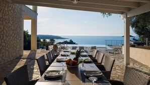 Un espace extérieur abrité, aménagé pour les repas, avec une table pour deux personnes, offrant une vue panoramique sur la mer.