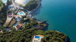 Vue aérienne d’une station balnéaire dotée de plusieurs piscines, d’une côte rocheuse et d’une végétation luxuriante.