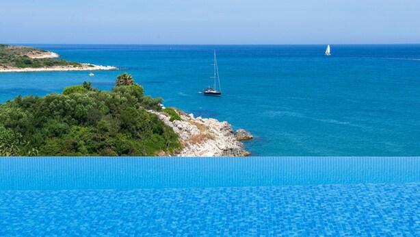 Une piscine d’un bleu éclatant, avec vue sur la mer et les bateaux.