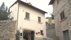 A two-story building with a stone facade, a small balcony, and a ground-level entrance with a wooden door. - Casa Stefy - Apartment in Cortona, Tuscany (Cortona)