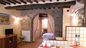 A rustic room with a stone archway leading to a bedroom, a wooden cabinet with a television, and a tiled bathroom area. - Casa Stefy - Apartment in Cortona, Tuscany (Cortona)