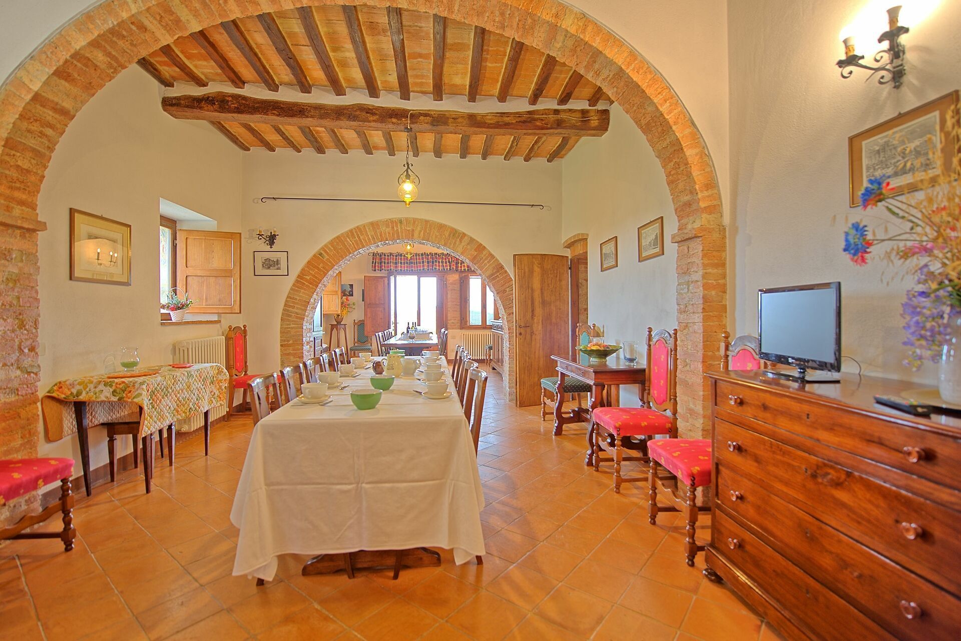 A dining area with a long table set for a meal, flanked by wooden chairs and a wooden cabinet with a television.