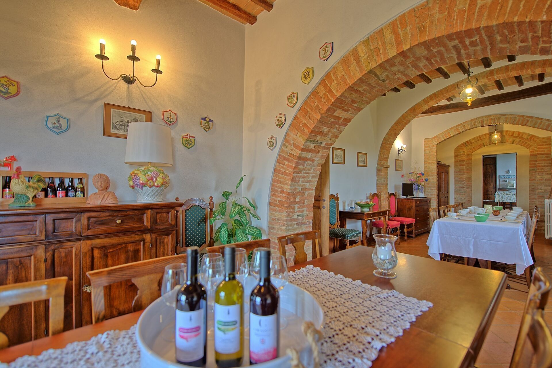 A dining area with a long table set for a meal, surrounded by brick arches and wooden furniture.