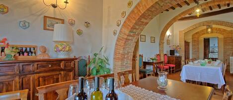 A dining area with a long table set for a meal, surrounded by brick arches and wooden furniture.