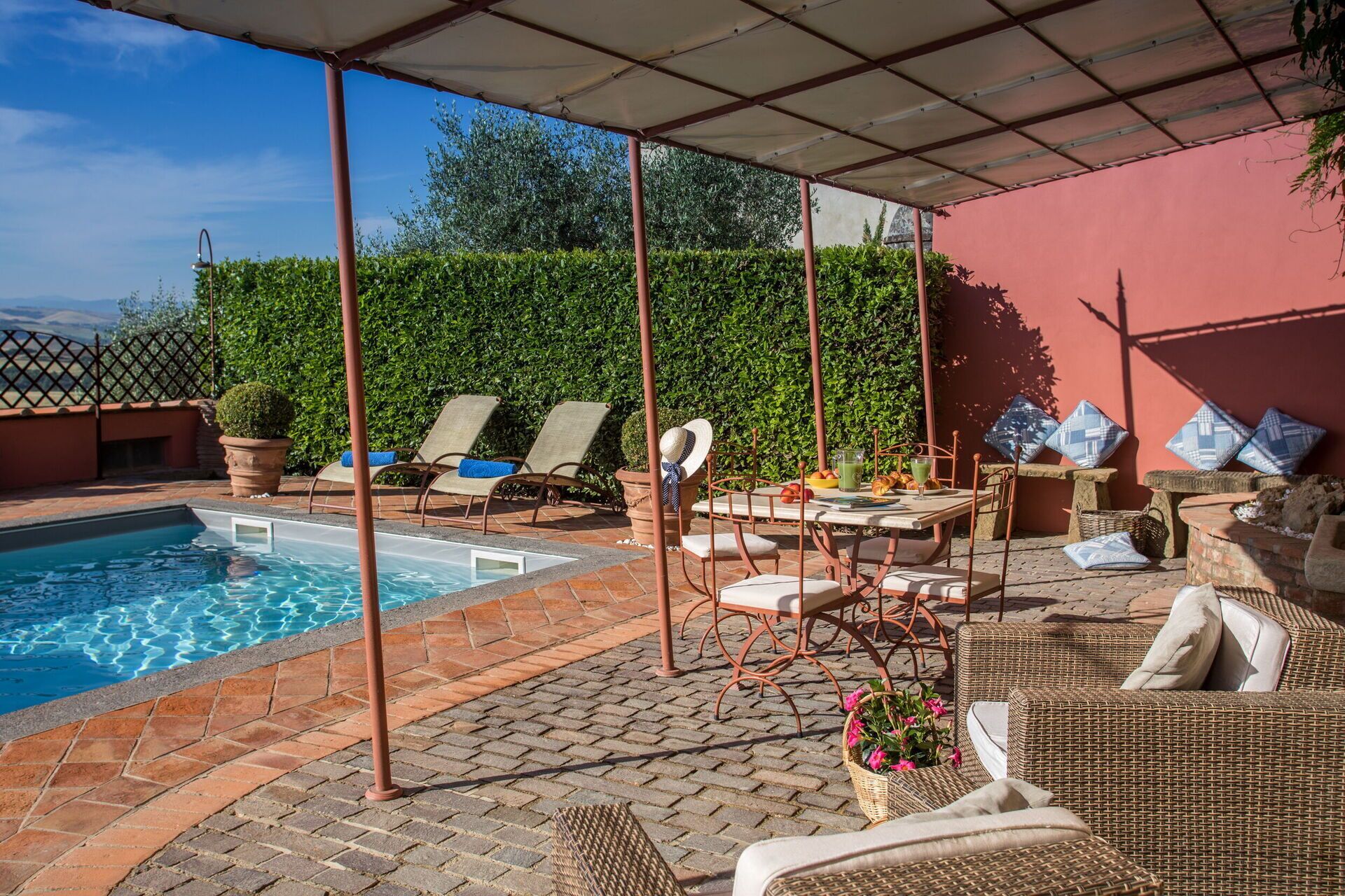 Zona de piscina con piscina, sillas de descanso, una mesa con bebidas y un porche cubierto.