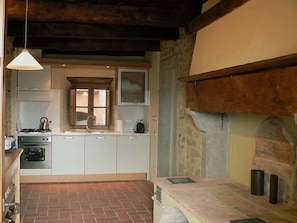 Une cuisine rustique avec un mur en pierre, des poutres en bois, un sol en briques et un luminaire suspendu.