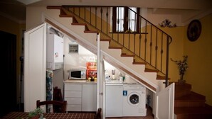 Une cuisine compacte équipée d’un four à micro-ondes, d’un évier et d’un lave-linge, un coin repas avec une table et des chaises, et un escalier menant à l’étage supérieur.