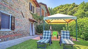 Un bâtiment en pierre doté d’un patio avec jardin, comprenant deux chaises et une table placées sous une pergola.