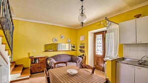 Un coin repas avec une table dressée pour deux personnes, une cuisine avec des meubles blancs et un escalier avec des marches en bois.