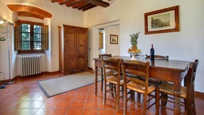 Un coin repas avec une table et des chaises en bois, un radiateur, une fenêtre donnant sur un paysage agréable et un tableau encadré au mur.
