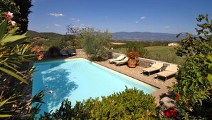 Une piscine entourée de chaises longues et agrémentée de plantes en pot, le tout niché au milieu de la verdure, avec des collines en arrière-plan.
