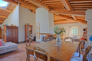 Enjoy meals in this inviting dining area with a long table, comfortable chairs, and a beautiful vase with flowers.