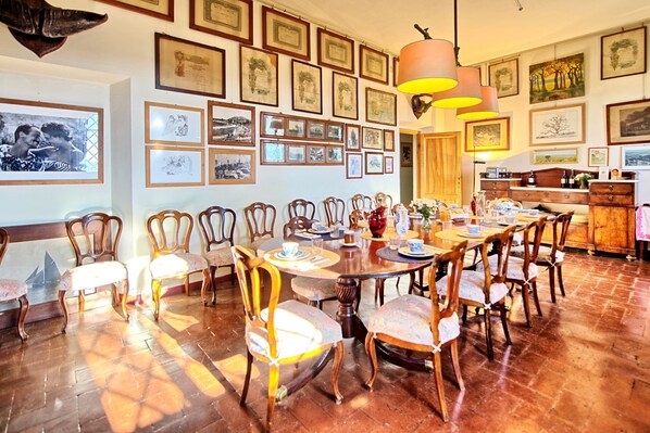 Un espace repas avec une longue table en bois, plusieurs chaises et des certificats encadrés accrochés au mur.