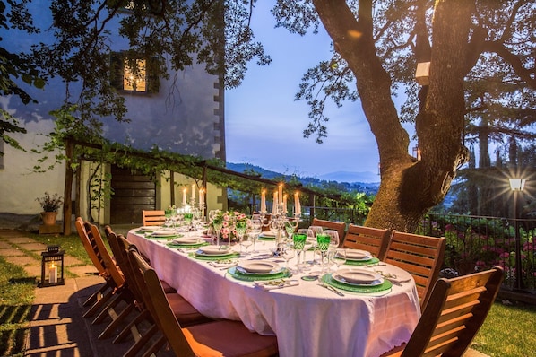 An outdoor dining area with a table set for six, surrounded by wooden chairs.