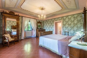 Une chambre à coucher avec un grand lit, une commode en bois, une chaise, un miroir et un lustre.