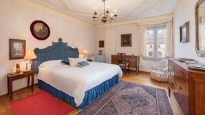 A bedroom with a large bed, a chandelier, a desk, a chair, and a dresser.