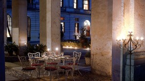 An outdoor dining area with a table set for four, surrounded by chairs with red cushions.