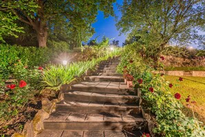 A stone staircase surrounded by lush greenery and flowering plants, leading up a hill.