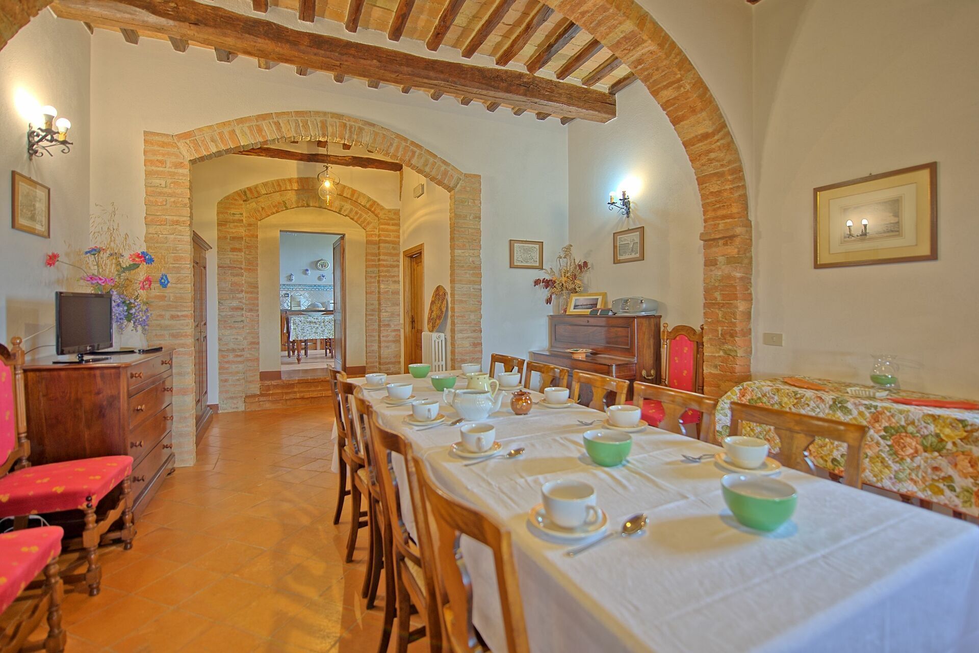 A dining area with a long table set for a meal, wooden chairs, and a brick archway leading to another room.