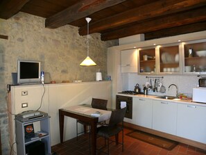 A compact kitchen with a stone wall, a dining table with chairs, a small TV, and basic appliances.