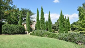 Un jardín bien cuidado con altos cipreses, un edificio de piedra y diversos arbustos.