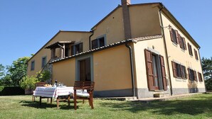 A two-story house with a balcony, a dining table set outdoors, and a grassy lawn. - Amiata - Vacation Rental in Orcia Valley, Tuscany (Centeno)