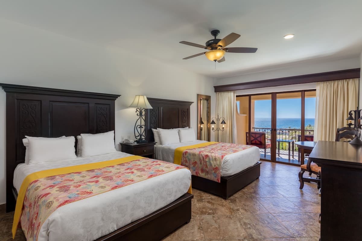 A hotel room with two beds, a ceiling fan, a balcony with a view, and a desk with a chair.
