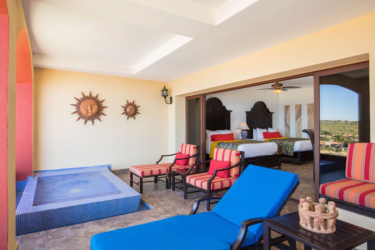 A room with a bed, a sun-shaped wall decoration, a ceiling fan, and a view of the landscape.